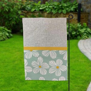May include: A gray and white garden flag with a yellow stripe and a pattern of white flowers on a light blue background.