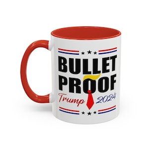 Peut inclure: Une tasse à café en céramique blanche avec un bord rouge. La tasse présente un motif noir et blanc qui dit "Bullet Proof Trump 2024" avec une cravate rouge et des cheveux jaunes sur le dessus. Le motif est entouré de rayures rouge, blanche et bleue.