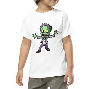 Puede incluir: Camiseta blanca para niños pequeños con un diseño de zombi de dibujos animados. El zombi tiene piel verde, ojos amarillos y pelo morado. Lleva una chaqueta gris y pantalones morados. El niño también lleva un gorro beige.