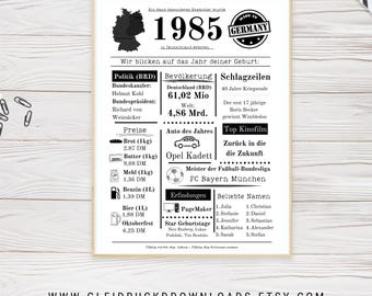 May include: A framed print with a cream-colored border, featuring German text and graphics. The design includes the year 1985, a map of Germany, and various facts and figures from that year. The Etsy shop URL is at the bottom.