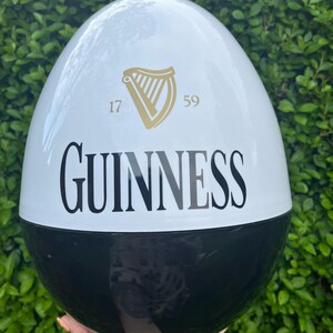 May include: A large, egg-shaped decorative item, split into black and white sections. The white section features the Guinness logo, a gold harp, and the numbers "17" and "59". The word "GUINNESS" is printed in large, black letters.