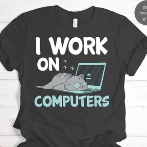 May include: A dark heather grey t-shirt with the text "I work on computers" in white. A cartoon cat is sleeping on a laptop computer.