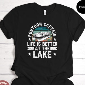 May include: Black t-shirt with a graphic that reads "PONTOON CAPTAIN" above an illustration of a pontoon boat. The text "LIFE IS BETTER AT THE LAKE" is below the boat illustration. The shirt has a crew neck and short sleeves.