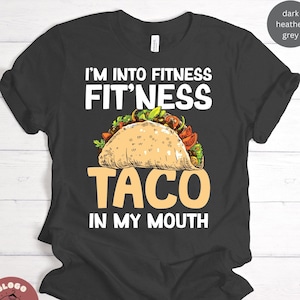 May include: Dark heather grey t-shirt with a graphic of a taco and the text "I'm into fitness Fit'ness Taco in my mouth".