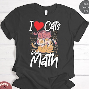 May include: Dark heather grey t-shirt with a graphic of three cats stacked on top of each other. The cats are surrounded by math equations. The text "I love cats and math" is printed on the shirt.