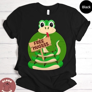 May include: Black t-shirt with a green cartoon snake holding a sign that says "Free Hugsss".