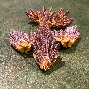 May include: A small, brown, and orange figurine of a mythical creature with wings and a spiky tail. The creature has blue eyes and a pointed snout.