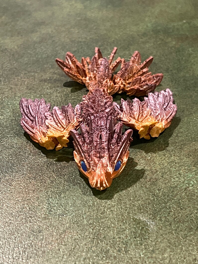 May include: A small, brown, and orange figurine of a mythical creature with wings and a spiky tail. The creature has blue eyes and a pointed snout.