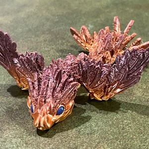 May include: A 3D printed, brown and gold, dragon-like creature with blue eyes and feathery wings.