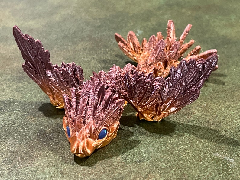 May include: A 3D printed, brown and gold, dragon-like creature with blue eyes and feathery wings.