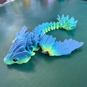 May include: A blue and green 3D printed dragon figurine with a segmented body and feathery wings.