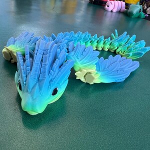 May include: A blue and green segmented toy with a spiky head. The toy is made of plastic and has a textured surface.