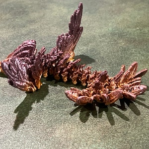 May include: A 3D printed, segmented, dragon-like sculpture with a metallic finish. The sculpture is made of multiple pieces that are connected together. The sculpture is painted in shades of brown and purple.