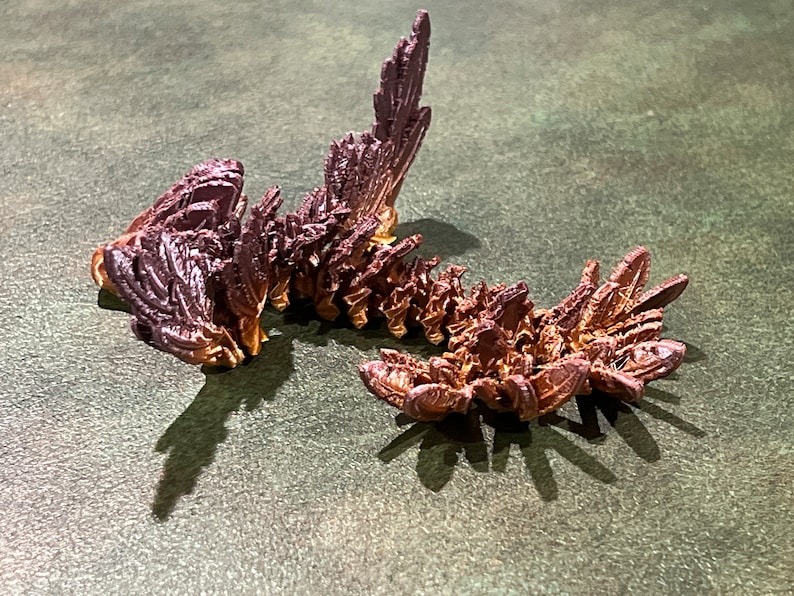 May include: A 3D printed, segmented, dragon-like sculpture with a metallic finish. The sculpture is made of multiple pieces that are connected together. The sculpture is painted in shades of brown and purple.