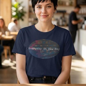 May include: Navy blue t-shirt with an oval design featuring lines of code in various colors. The text "Everyday Is Dev Day" is displayed in white. The shirt is made of a soft material.