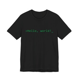 May include: Black t-shirt with the text ">Hello, world!_" in green. The shirt has a crew neck and short sleeves. The text is in a monospace font, commonly used in programming.