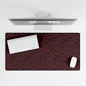 May include: A rectangular desk mat with a burgundy and black floral pattern. A white keyboard and mouse are on the mat. A computer monitor is above the mat.