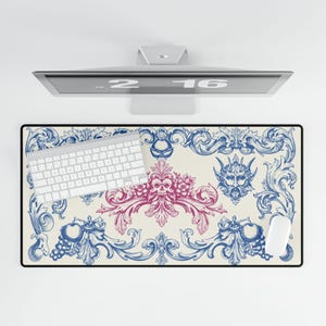 May include: A rectangular desk mat with a black border, featuring a cream-colored background and a blue and pink baroque design. A white keyboard and mouse are on the mat.