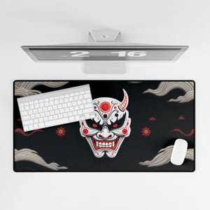 Peut inclure: Tapis de bureau rectangulaire noir avec un motif de masque Oni blanc et rouge. Un clavier et une souris blancs sont sur le tapis. Le fond comprend des nuages stylisés et des accents floraux rouges. Un écran d'ordinateur est au-dessus du tapis.