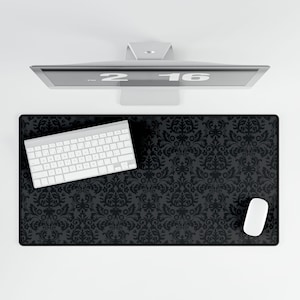 Può includere: Vista dall'alto di una configurazione del computer con un tappetino per scrivania nero con motivo damascato, una tastiera bianca e un mouse bianco. Un monitor del computer argentato mostra l'ora. Il tappetino offre uno spazio di lavoro elegante e funzionale.