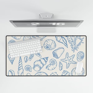 May include: A rectangular desk mat with a black border featuring a cream background and blue seashell illustrations. A white keyboard and mouse are on the mat. A computer monitor is above the mat.