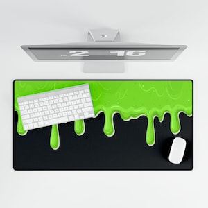 Puede incluir: Alfombrilla de ratón rectangular negra con un diseño de baba verde, un teclado blanco y un ratón blanco. La baba verde gotea desde la parte superior de la alfombrilla. El teclado está situado en el lado izquierdo.