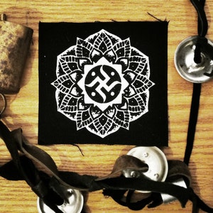 May include: Black fabric patch with a white mandala design featuring a stylized symbol in the center. The symbol is a stylized swastika with two fish inside.