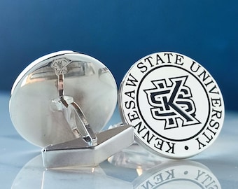 May include: Silver cufflinks with a black and white logo of Kennesaw State University. The cufflinks are round and have a silver finish.