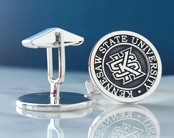 May include: Silver cufflinks with a black and white circular design featuring the text "Kennesaw State University" and a stylized "K" logo.