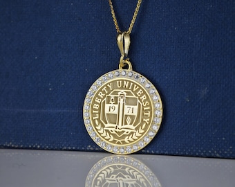 May include: Gold pendant necklace with a round charm featuring the Liberty University logo and a border of small clear stones. The logo includes the words "Liberty University" and the years "1971".