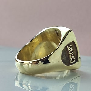 Puede incluir: Un anillo de oro con una cara cuadrada y el año 2023 grabado en el lateral. El anillo está marcado con 14K en el interior.