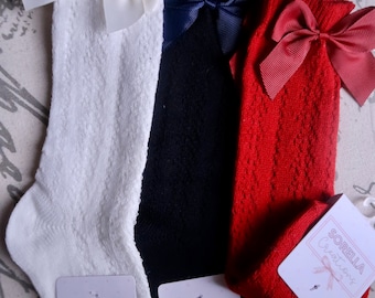 Puede incluir: Tres pares de calcetines hasta la rodilla con lazos. Los calcetines son blancos, negros y rojos. Cada par tiene un lazo de un color diferente. Los calcetines están hechos por Sorella Creations.