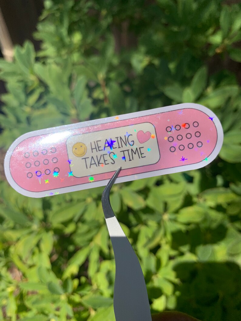 May include: Pink plaster sticker with glitter and the text "Healing Takes Time" with a smiley face and a heart.