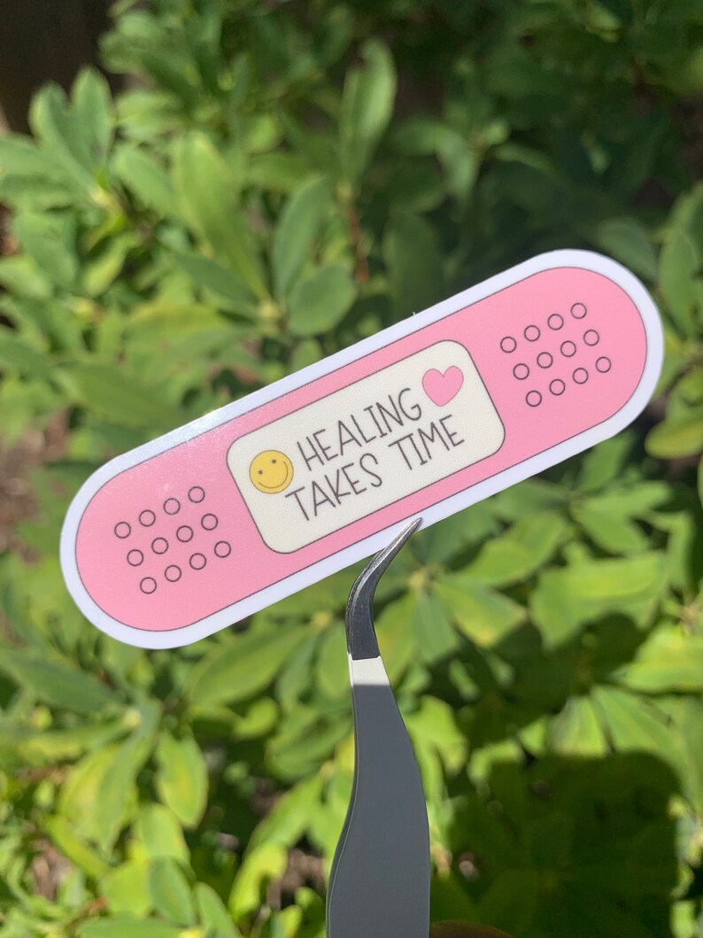 May include: Pink plaster sticker with a smiley face, a pink heart, and the text "HEALING TAKES TIME".