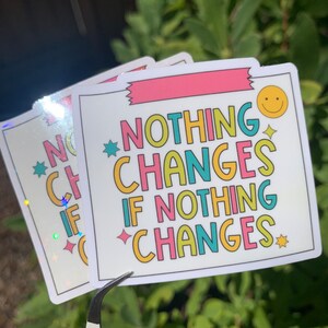 May include: A white sticker with a pink, yellow, blue, and green design. The sticker says "Nothing Changes If Nothing Changes" with a smiley face in the corner.