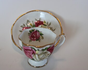 May include: A white teacup and saucer with a gold rim and floral pattern featuring pink and white roses.
