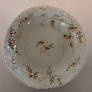 Puede incluir: Un tazón de porcelana blanca con un borde festoneado y un diseño floral. El tazón está decorado con delicadas flores marrones y amarillas.