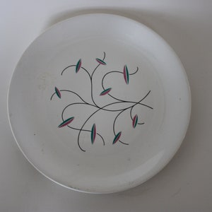 May include: White ceramic plate with a black and green floral design. The design features stylized leaves and flowers with pink accents.