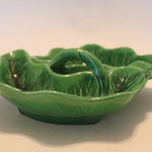 May include: A green ceramic serving dish shaped like a cabbage leaf with three individual sections. The dish has a handle in the center.