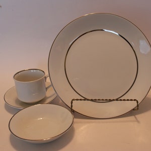 May include: A set of white ceramic dishes with a gold trim. The set includes a cup, saucer, bowl, and a larger plate.