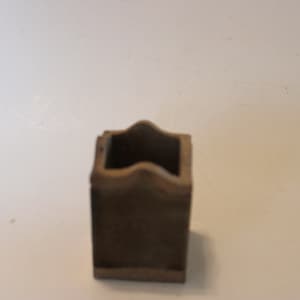 May include: A small, square, brown ceramic planter with a wavy rim.