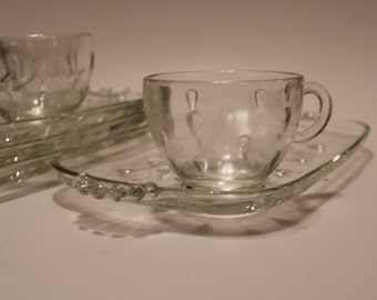 May include: A set of clear glass teacups and saucers with a textured, bubble-like design. The cups and saucers are stacked on top of each other.