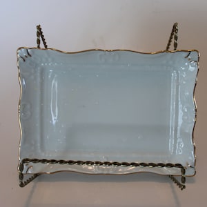 May include: A white porcelain tray with a gold trim and a delicate floral design. The tray is on a gold metal stand.