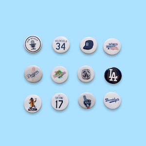 May include: A collection of twelve round pinback buttons with various designs and text. The buttons feature baseball-themed graphics, including team logos, player numbers, and the words "World Series" and "Dodgers". The background is a light blue.