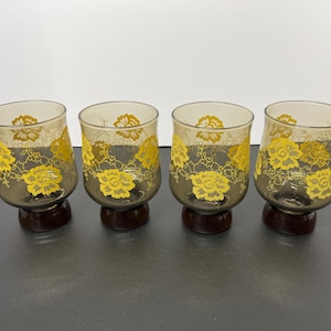 May include: Set of four brown glass drinking glasses with yellow floral designs. The glasses have a short stem and a wide base.