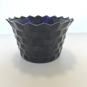 May include: A dark blue decorative bowl with a geometric, basket-weave pattern. The bowl has a scalloped rim and a deep blue interior. The design is modern and the bowl is likely made of glass or ceramic.