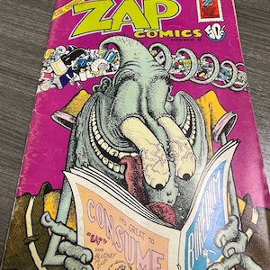 May include: A vintage comic book cover featuring a green monster with a large mouth and a tongue sticking out. The monster is reading a newspaper with the headline "It's Great to Consume" and the text "Eat" in quotation marks. The comic book is titled "Zap Comics" and is number 6. The cover is pink with a yellow border.