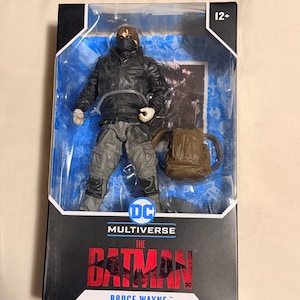 May include: A boxed action figure of Bruce Wayne from "The Batman" movie. The figure is wearing a black jacket, gray pants, and a face covering. A brown backpack is included. The box features the DC Multiverse logo and the movie title.