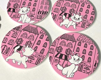May include: Set of four pink and black ceramic coasters featuring a cartoon cat walking down a street with buildings and a cafe. The cat is wearing a bow and has a white body with black markings.