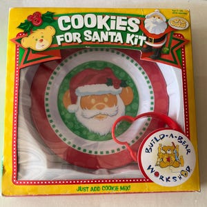 May include: A Build-A-Bear Workshop Cookies for Santa Kit. The kit includes a plate and cookie cutter with a Santa Claus design. The box is yellow with red and green accents and the text "Cookies for Santa Kit".
